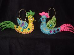 two colorful birds sitting next to each other on a black cloth covered surface with beads and sequins