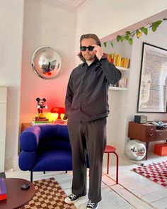 a man standing in the middle of a living room talking on his cell phone while wearing sunglasses