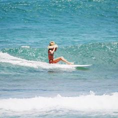 a woman riding a surfboard on top of a wave in the ocean with a hat