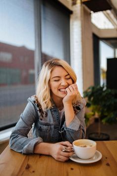 a woman sitting at a table with a cup of coffee in her hand and smiling