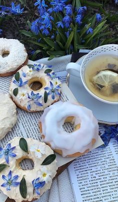 doughnuts with white frosting and blue flowers next to a cup of tea