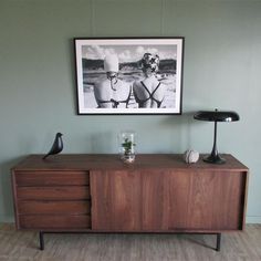 a wooden sideboard with two lamps on top of it and a framed photograph above it