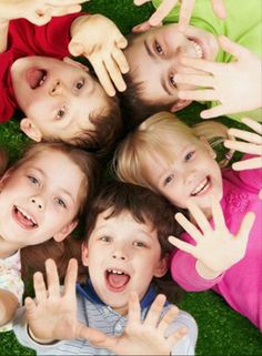 a group of children laying in the grass with their hands up