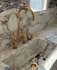 a marble sink with gold faucets in the middle and windows above it, next to a window sill