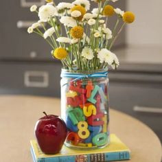 a jar filled with letters and flowers on top of a table next to an apple