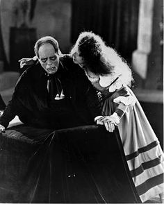 an old black and white photo of two people dressed in costumes looking at each other