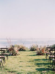 chairs are set up in the grass for an outdoor wedding ceremony with flowers and greenery