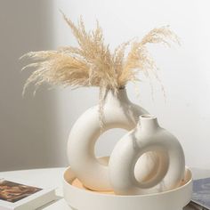 two white vases sitting on top of a table next to a book and magazines