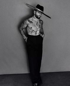 a man with tattoos and a hat standing in front of a wall