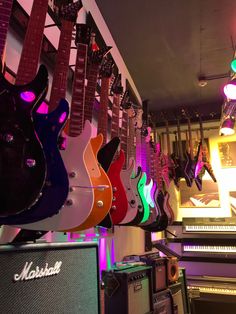 guitars and amps are lined up in a music store with neon lights on the walls