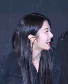 a woman with long black hair laughing and looking to the side while wearing a denim jacket