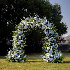 an arch made out of blue and white flowers in the middle of a grassy area