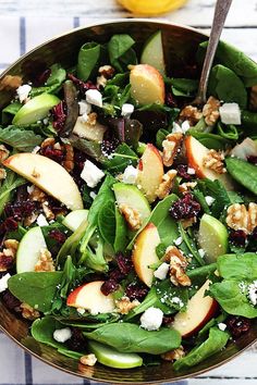 a salad with spinach, apples, walnuts and feta cheese in a bowl