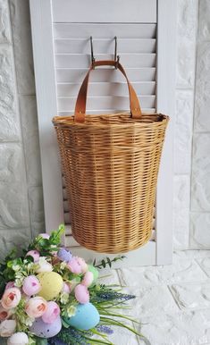 a basket hanging from the side of a wall with flowers and eggs in front of it