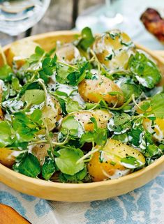 a wooden bowl filled with salad on top of a blue and white table cloth next to utensils