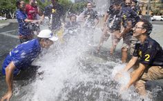 a group of people standing around a fountain with water shooting out of it's sides