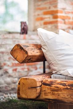 a wooden bench with white pillows on it in front of a brick wall and window