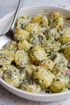 a white bowl filled with potato salad on top of a table next to a spoon