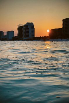 the sun is setting over some buildings in the water