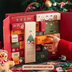 a person is holding an apple calendar gift box in front of a christmas tree and teddy bear