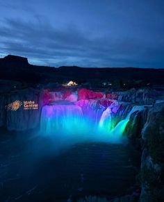 the waterfall is lit up at night with colorful lights on it's sides and water cascading down its sides