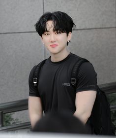 a young man with black hair is standing in front of a building