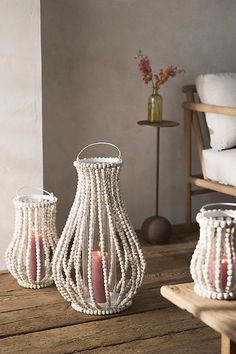 three white beaded vases with candles on a wooden table next to a chair