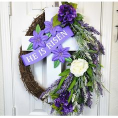 a wreath with purple flowers and he is risen written on it, hanging on the front door