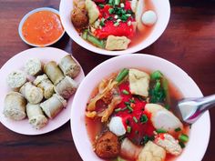 three bowls filled with different types of food on top of a wooden table next to dipping sauce