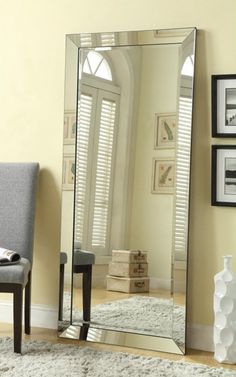 a large mirror sitting on top of a wooden floor next to a chair and window