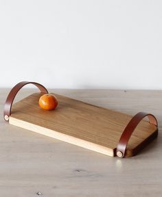 an orange sitting on top of a wooden cutting board next to a pair of leather straps