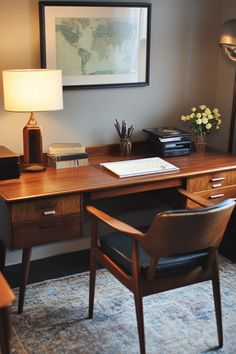 a wooden desk topped with a computer monitor next to a lamp