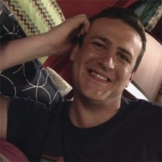 a man smiling and holding his hair in one hand while sitting on the floor next to a couch