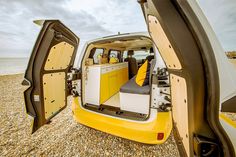 the interior of a van with its doors open on a gravel beach near the ocean