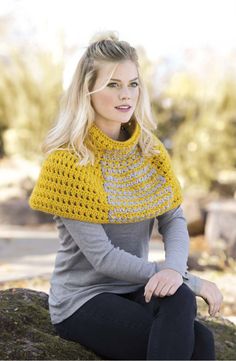 a woman sitting on top of a rock wearing a yellow and gray crocheted scarf