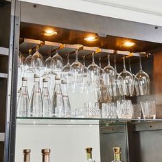 many empty wine glasses are lined up on the shelf in front of some liquor bottles