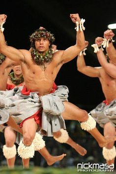 a group of men dancing on stage with their hands in the air and wearing leis