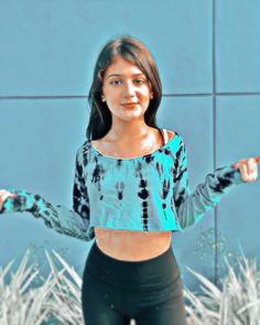 a woman with her arms out in front of a blue wall wearing black leggings and a tie dye crop top