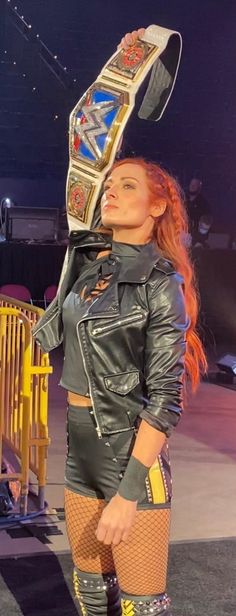 a woman in leather pants and boots holding a wrestling belt on top of her head