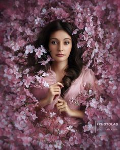 a woman is surrounded by pink flowers with her hands on her chest and looking at the camera