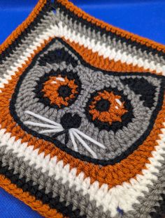 an orange and white crocheted square with a black cat on it's face