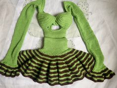 a green and brown knitted dress on a white bed with a lace doily