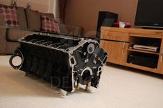 an engine block sitting on the floor in front of a table with a tv and couch behind it