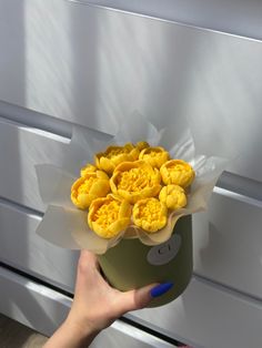 a person holding a green container with yellow flowers in it