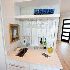 a kitchen counter with wine glasses, bottles and a pear on it next to a sink