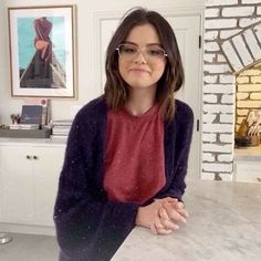 a woman wearing glasses sitting at a counter in front of a brick wall and fireplace