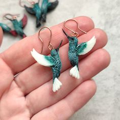 a pair of hummingbird earrings in the palm of someone's hand