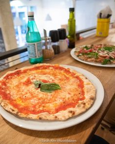 two pizzas sitting on top of white plates on a wooden table next to bottles