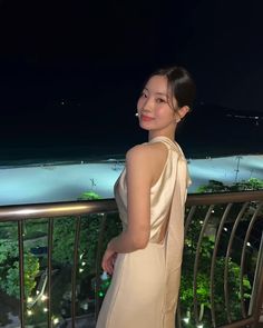 a woman standing on top of a balcony next to a night time sky line with the ocean in the background