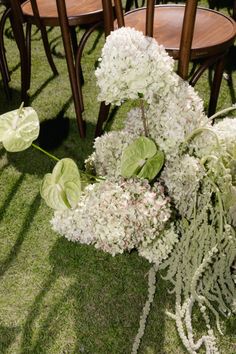 white flowers and greenery sit on the grass near wooden chairs at an outdoor event